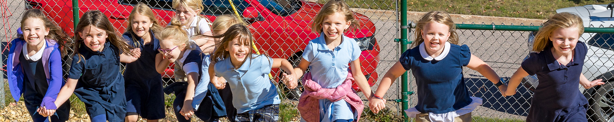 A group of smiling girls holding hands and running together outside