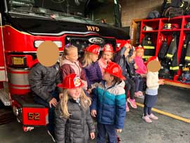 Students in fire hats at the front of a fire engine