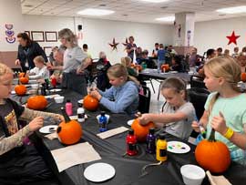 Adults helping students paint on pumpkins