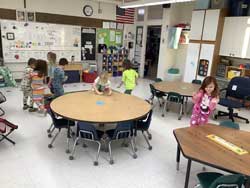 students moving around tables in the classroom