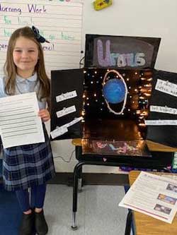 girl holding paper next to a display about Uranus