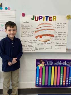 boy standing next to his poster about Jupiter.