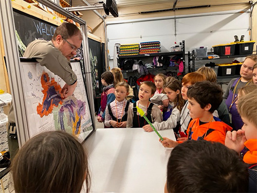 Students listening to an adult talk about a map
