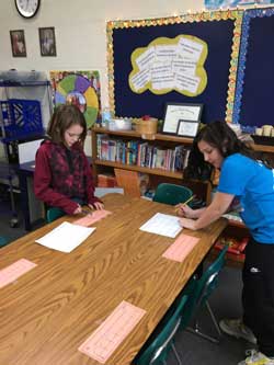 Two girls standing at table and writing on papers