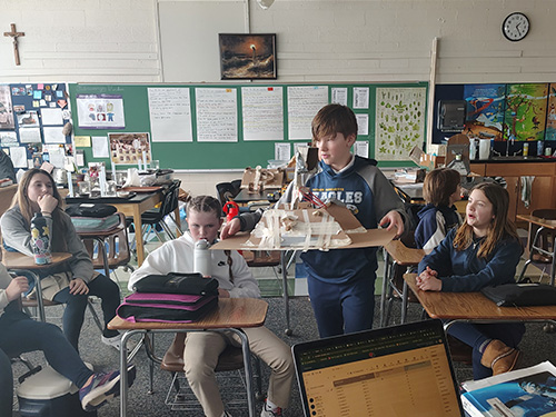 A student bringing a cardboard display to the front of the classroom