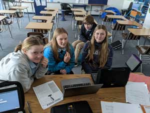 four students around table with laptops and papers on it