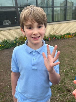 Little second grade boy in a short sleeve light blue shirt with a ladybug on his finger.
