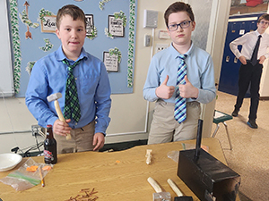 Two fifth grade boys dressed in colonial attire next to hammers and nails on table