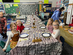 Students in costume sitting at medieval dinner table in the classroom