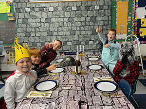 Students in costume sitting at medieval dinner table and giving a thumbs up