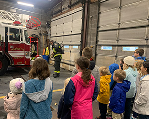 Students watching fireman put on his gear next to the firetruck