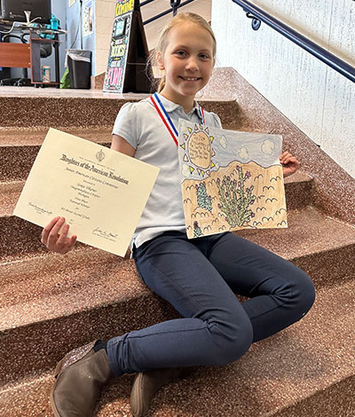 Sonja Yikaner holding her award for first place national winner for her 2nd grade art poster