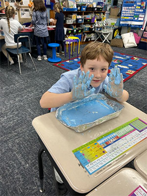 Student holding up his hands full of blue oobleck