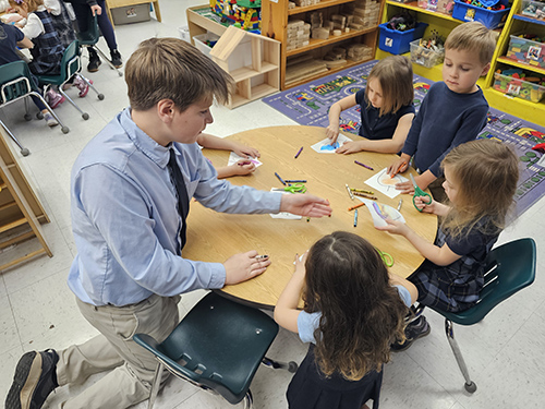 Pre-k students enjoying a coloring activity led by an older student