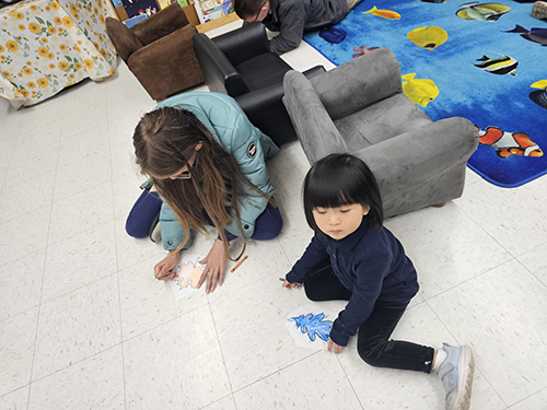 Two girls coloring together on the classroom floor