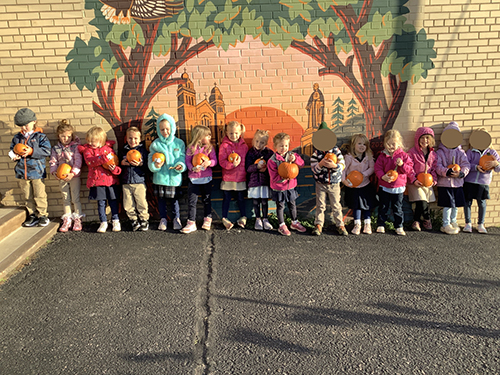 Pre-kindergarten students holding their pumpkins in front of a pretty mural