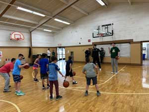 students dribbling basketballs in gym in front of coaches