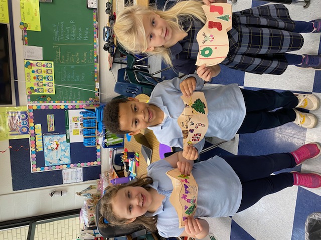 Three students holding up their wooden shoe artwork